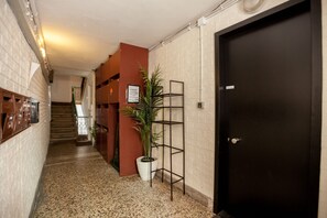 A hallway with a black door, a potted plant, and a metal shelf unit.