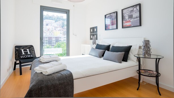 A modern hotel room with a large bed, a view of the city, and a chair with a "H HOME" sign. - FLH Martim Moniz Castle View Flat (Lisbon)
