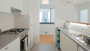 A modern kitchen with white cabinets, a gas stove, a sink, and a window overlooking a balcony. - FLH Martim Moniz Castle View Flat (Lisbon)