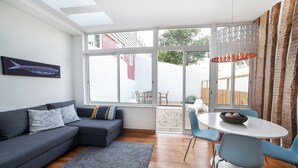 Ein modernes Wohnzimmer mit einem grauen Sofa, einem Esstisch mit Stühlen und einem großen Fenster mit Außenblick.
