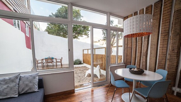 Ein modernes Wohnzimmer mit großem Fenster, einem Essbereich mit blauen Stühlen und einem grauen Sofa.