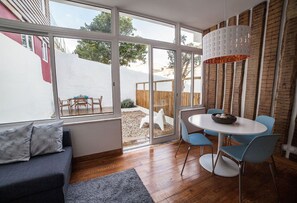 A modern living room with a large window, a dining area with blue chairs, and a grey sofa.
