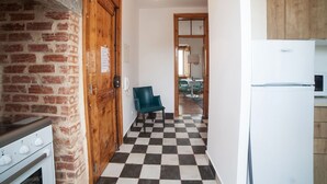A narrow hallway with a checkered floor, a wooden door, a blue chair, and a white refrigerator. - FLH Lisbon Sun Terrace Graça III (Lisbon)