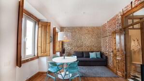 A cozy room with a round table and chairs, a dark sofa, and a stone wall. - FLH Lisbon Sun Terrace Graça III (Lisbon)