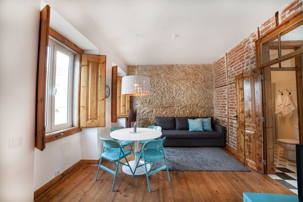 A cozy room with a round table and chairs, a dark sofa, and a stone wall.