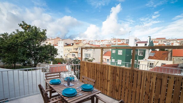 A wooden table set with blue plates and wine glasses on a balcony with a view of buildings. - FLH Lisbon Sun Terrace Graça III (Lisbon)