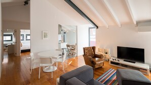 A modern living room with a flat-screen TV, leather armchair, and a dining area with a white table and chairs. - FLH Bairro Alto Balcony Flat (Lisbon)