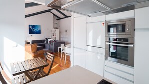 A modern kitchen with white cabinetry, a built-in oven, and a dining area with a wooden table and chairs. - FLH Bairro Alto Balcony Flat (Lisbon)