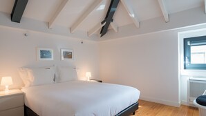 A bedroom with a large bed, two bedside tables with lamps, wooden flooring, and a window with blinds. - FLH Bairro Alto Balcony Flat (Lisbon)