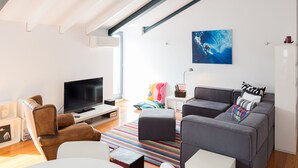 A modern living room with a flat-screen TV, a gray sofa, a white dining table, and a colorful rug. - FLH Bairro Alto Balcony Flat (Lisbon)