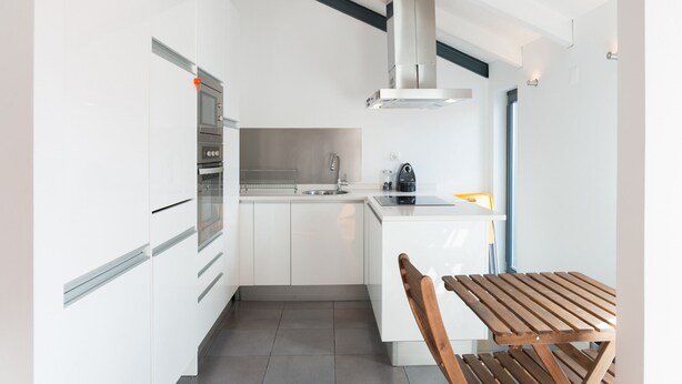 A modern kitchen with white cabinetry, a built-in oven, a sink, and a wooden table. - FLH Bairro Alto Balcony Flat (Lisbon)