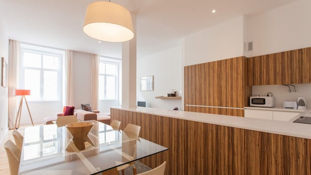 A modern kitchen with a wooden accent wall, a glass dining table, and a pendant light. - FLH Baixa Spacious Apartment (Lisbon)