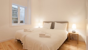 A double bed with white linens and two pillows, a bedside table with a lamp, and a window with blinds. - FLH Baixa Spacious Apartment (Lisbon)