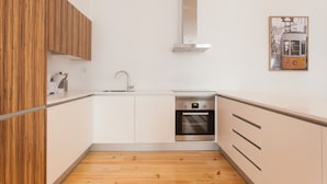A modern kitchen with white cabinets, a wooden floor, a stainless steel oven, and a small sink. - FLH Baixa Spacious Apartment (Lisbon)
