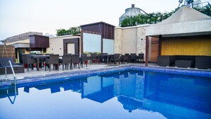 A swimming pool with lounge chairs and tables, surrounded by buildings with modern architecture. - Hotel Almeida (Dera Bassi)