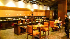 A restaurant with wooden furniture, a buffet setup, and a decorative wall. - Hotel Almeida (Dera Bassi)