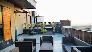 A rooftop terrace with wicker furniture, potted plants, and a view of the cityscape. - Hotel Almeida (Dera Bassi)