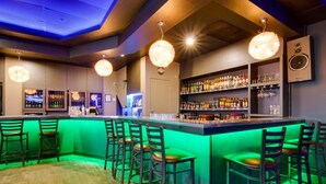 Eine Bar mit einer beleuchteten Theke in Grün, mehreren Barhocker und einer Auswahl an Spirituosenflaschen in Regalen.