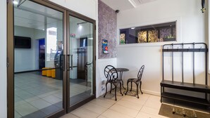 Ein modernes Interieur mit Glastür, einer kleinen Sitzecke mit zwei Stühlen und einer Bank, sowie einem dekorativen Wandbild.