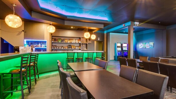 Eine Bar mit beleuchteter Theke, mehreren Sitzgelegenheiten und hängenden, kugelförmigen Leuchten.