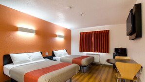 Ein Hotelzimmer mit zwei Betten, einem Schreibtisch, einem Stuhl, einem Fernseher und einem Fenster mit Vorhängen.