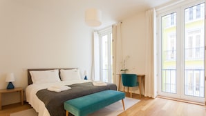 A modern bedroom with a bed, bench, bedside tables, and a view of the outside.