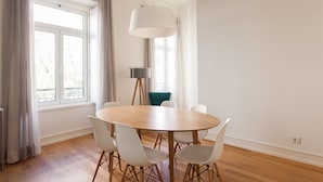 A dining area with a round table, white chairs, a floor lamp, and a window with curtains.