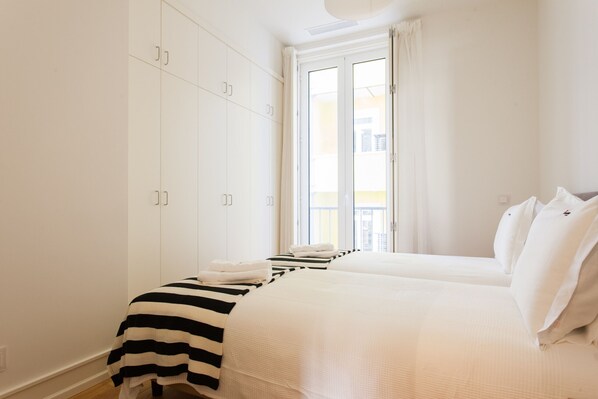 A hotel room with a large wardrobe, a bed with white bedding, and a view of the outside through a window.