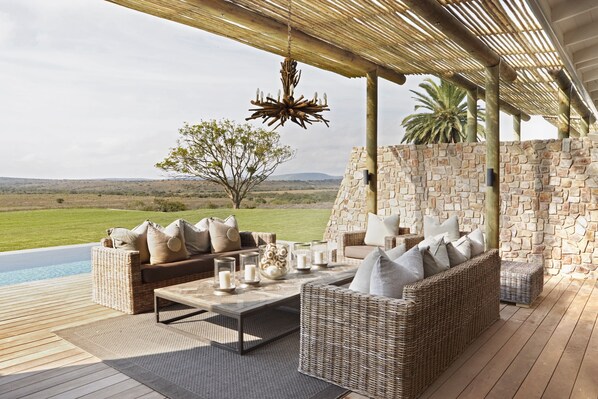 Un espacio al aire libre con mobiliario de mimbre, una piscina y un muro de piedra de fondo.