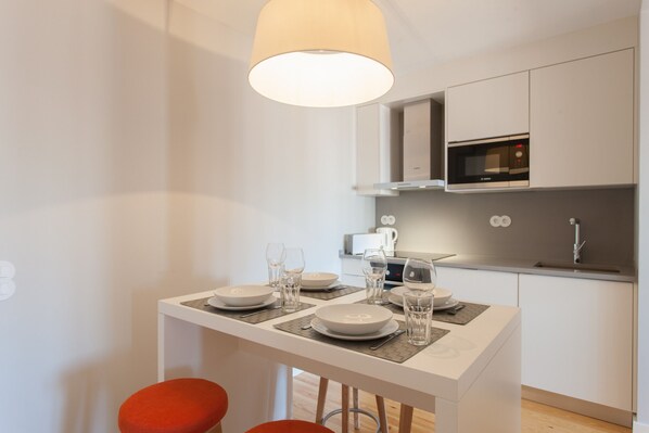 Une cuisine moderne avec des armoires blanches, un four à micro-ondes encastré et un coin repas avec une table dressée pour deux personnes.