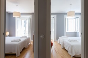 A hotel room with two beds, a wooden floor, a white door, and a window.