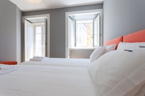 Une chambre d’hôtel avec deux lits, une tête de lit rouge et une fenêtre donnant sur des immeubles.