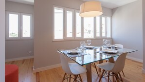A dining area with a glass table, white chairs, and a hanging light fixture. - FLH Príncipe Real Luxus Apartment II (Lisbon)