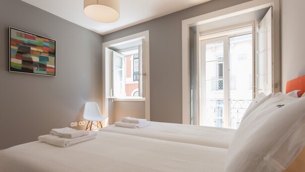 A hotel room with two beds, a painting on the wall, a lamp, and a view of the outside. - FLH Príncipe Real Luxus Apartment II (Lisbon)