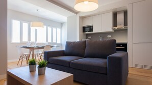A modern living room with a sofa, a dining table with chairs, and a kitchen area with cabinets and appliances. - FLH Príncipe Real Luxus Apartment II (Lisbon)