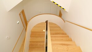 A wooden staircase with a glass handrail, white walls, and a ceiling with a sloped design. - FLH Porto Modern Rooftop (Oporto)