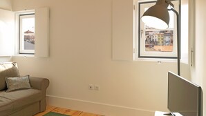 A room with a green carpet, a sofa with a patterned pillow, a desk with a computer, and a window with a view of buildings. - FLH Porto Modern Rooftop (Oporto)