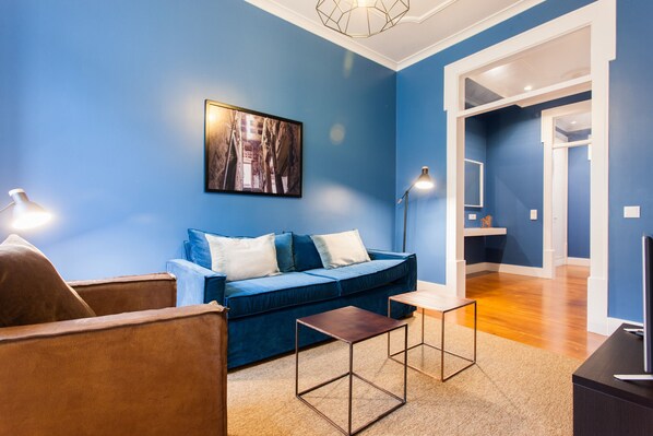 Una sala de estar con un sofá azul, dos sillones, una mesa de centro y un cuadro en la pared.