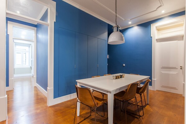 Un comedor con una mesa blanca y sillas marrones, paredes azules y una puerta blanca.