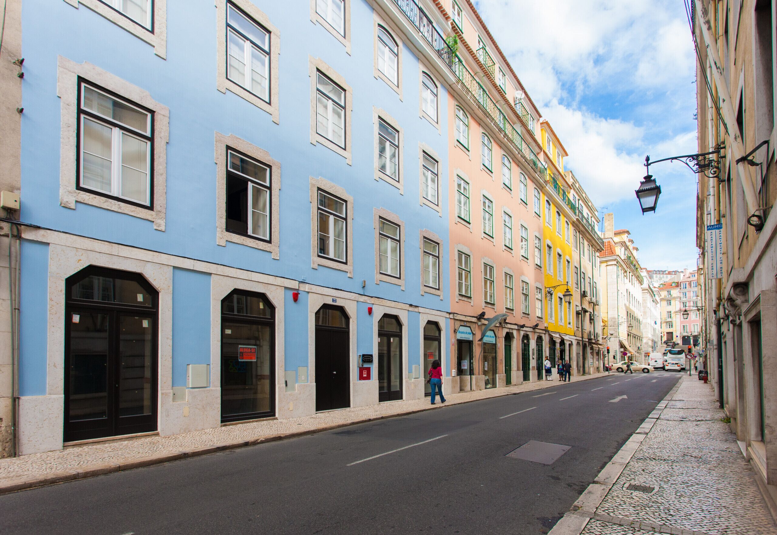 Una strada con edifici colorati, cielo sereno e un pedone.