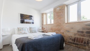 Une chambre à coucher avec un lit, une fenêtre, un mur en briques et un tableau accroché au mur.
