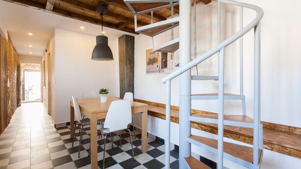 Un intérieur moderne avec un escalier en colimaçon, un coin repas doté d’un sol à carreaux et un luminaire suspendu.