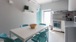 Une cuisine moderne avec des armoires blanches, un four encastré et un coin repas comprenant une table blanche et des chaises de couleur turquoise.