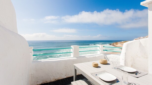 Un balcon blanc avec une table dressée pour deux personnes, donnant sur l’océan.