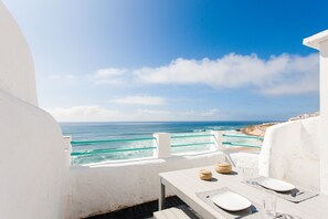Un balcon blanc avec une table dressée pour deux personnes, donnant sur l’océan.