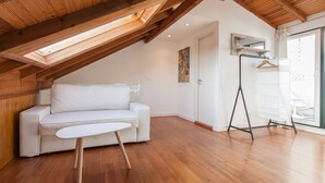 Ein modernes Schlafzimmer im Loft-Stil mit schrägem Dach, einem weißen Sofa, einem kleinen Tisch und Holzboden.