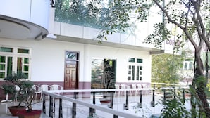 A modern building with a white facade, a balcony with white railings, and a potted tree. - Tuan Vu Hotel (Buon Ma Thuot)