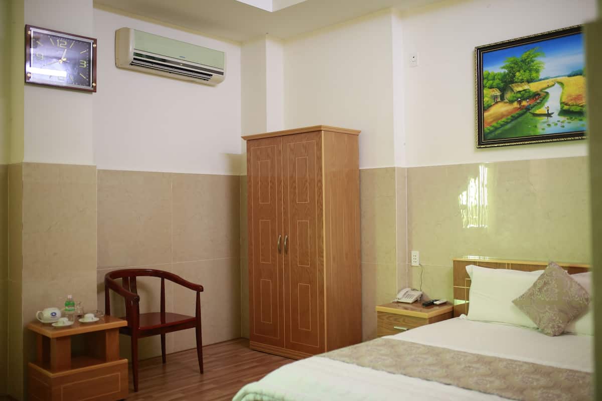 Une chambre d’hôtel avec une armoire en bois, une chaise en bois, une table de chevet avec un téléphone, un tableau au mur et une horloge.