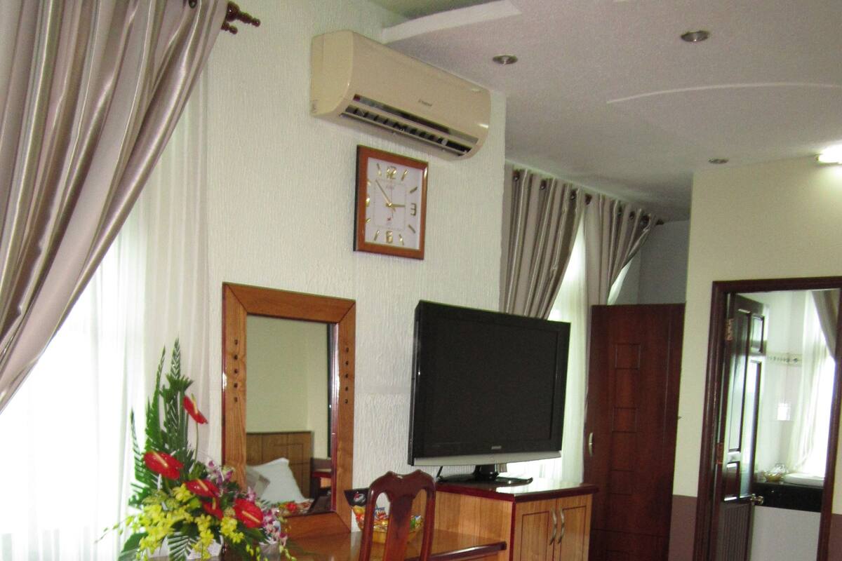 Une chambre d’hôtel avec un bureau en bois, une télévision, un lit et un miroir.