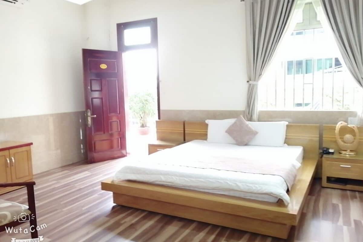 Une chambre à coucher avec un lit en bois, une table de chevet, une armoire en bois, une porte et une fenêtre avec des rideaux.